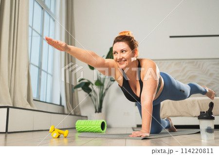 Yoga fitness workout training. Woman practicing yoga at home. Plus size female doing sports exercise on yoga mat indoor. Girl in sportswear have training workout for weight loss. Sport and fitness 114220811