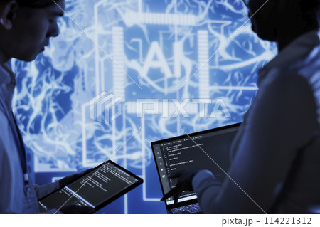 Hardworking colleagues write code on tablet and laptop to visualize artificial intelligence neural networks using augmented reality. Teamworking coworkers run AI script for information processing 114221312