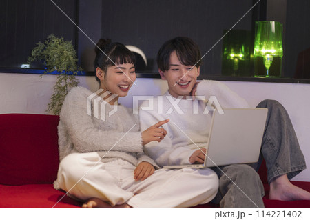 ソファに座ってパソコンの画面を見る笑顔の若い男女 114221402