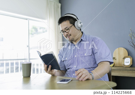 本を読みながら音楽を聴く大柄な日本人男性 114225668