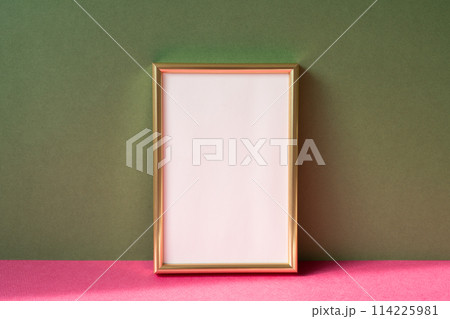Gold picture frame with copy space on pink table. khaki green wall background Gold picture frame with copy space on pink table. khaki green wall background 114225981