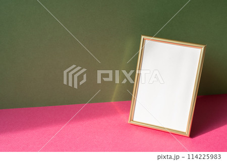 Gold picture frame with copy space on pink table. khaki green wall background Gold picture frame with copy space on pink table. khaki green wall background 114225983
