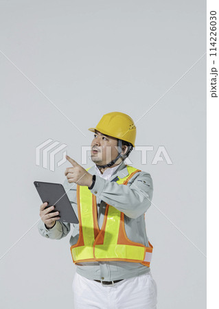 タブレット端末を見ながら指示を出す作業服の男性 114226030