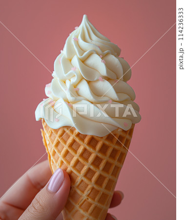Soft serve ice cream cone held against a pink background. 114236333