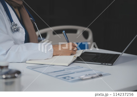 Female doctor sitting at desk and writing a prescription for her patient 114237256