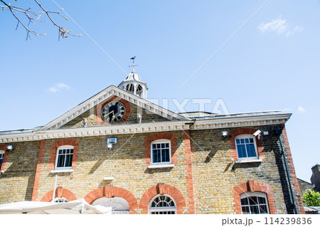 明るい日差しの下の大時計の付いた歴史的なレンガ造りの建物 ロンドンの西のラベンズコート公園にて 明るい日差しの下の大時計の付いた歴史的なレンガ造りの建物 ロンドンの西のラベンズコート公園にて 114239836