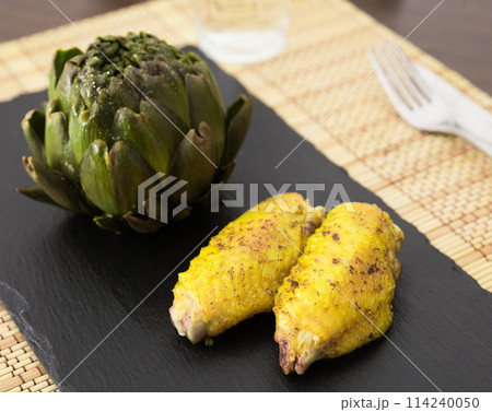 Cooked fried chicken wings and halves artichokes on black stone plate 114240050