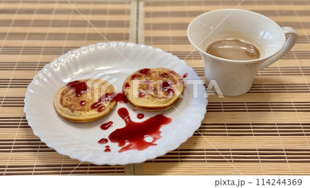 Healthy fritters with with lingonberry jam on a white ceramic plate next to white cup of coffee. Vegan breakfast food at the restaurant 114244369