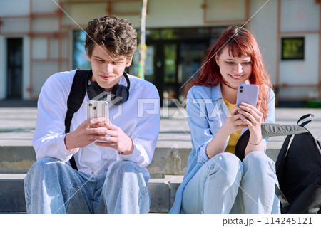 Teenage youth guy and girl college students sitting outdoor using smartphone 114245121