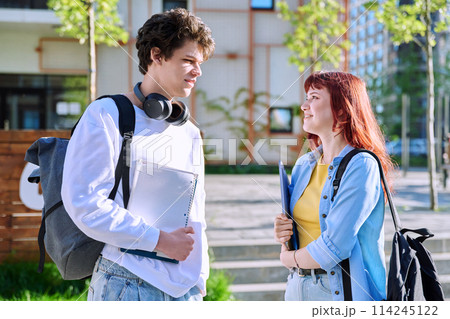 Teenage college students guy and girl talking, standing outdoor near educational building. Teenage college students guy and girl talking, standing outdoor near educational building. 114245122