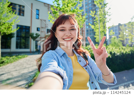 Selfie portrait of young happy red-haired female looking at camera outdoor Selfie portrait of young happy red-haired female looking at camera outdoor 114245124