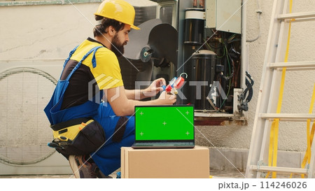 Seasoned mechanic employed by customer to find cause of faulty outdoor hvac system using measurement device, with nitrogen pressure loss over time displayed on chroma key laptop screen Seasoned mechanic employed by customer to find cause of faulty outdoor hvac system using measurement device, with nitrogen pressure loss over time displayed on chroma key laptop screen 114246026