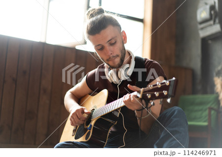 Handsome young man playing acoustic guitar sitting Handsome young man playing acoustic guitar sitting 114246971