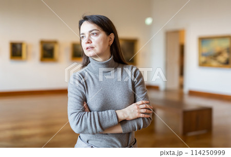 Interested woman visiting exhibition of paintings in art museum 114250999