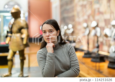Interested woman viewing collection of medieval armor in museum 114251026