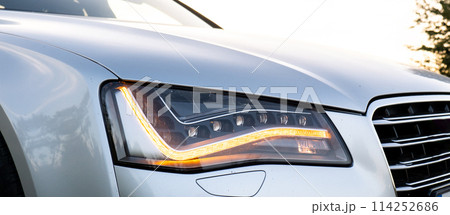 Headlight turned on in Clean car after Washing luxury silver car. Sedan car exterior of modern luxury car during sunset on highway road. Details of front headlamp. Prestige sport 114252686