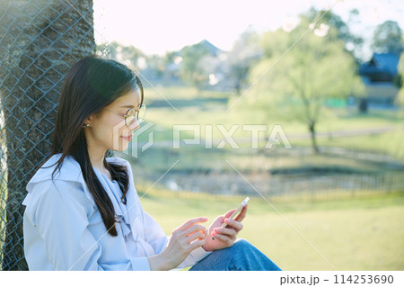 桜の下でスマートフォンを見る女性 114253690