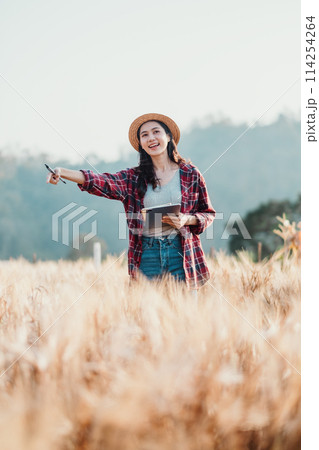 Enthusiastic farmer points out details in the wheat field while holding a digital tablet on a sunny day. 114254264