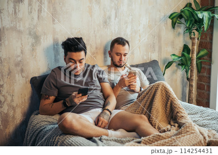 Happy gay couple taking selfie on bed at home Happy gay couple taking selfie on bed at home 114254431