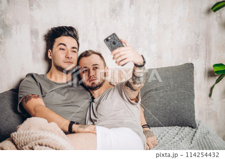 Happy gay couple taking selfie on bed at home Happy gay couple taking selfie on bed at home 114254432