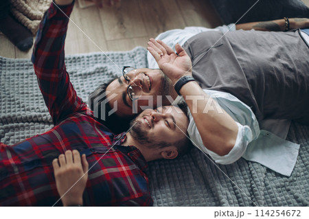 Happy cheerful caucasian gay couple wearing casual clothes making selfie on bed Happy cheerful caucasian gay couple wearing casual clothes making selfie on bed 114254672