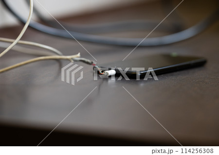 The smartphone is charging from a faulty cable. The concept of danger, the use of non-standard equipment, worn-out equipment The smartphone is charging from a faulty cable. The concept of danger, the use of non-standard equipment, worn-out equipment 114256308