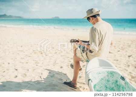 ハワイの砂浜で,ターコイズブルーの海をバックにウクレレをひく若い男性 114256798