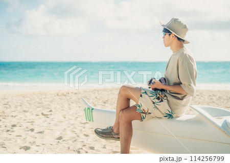 ハワイの砂浜で,ターコイズブルーの海をバックにウクレレをひく若い男性 114256799