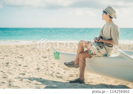 ハワイの砂浜で,ターコイズブルーの海をバックにウクレレをひく若い男性 114256802
