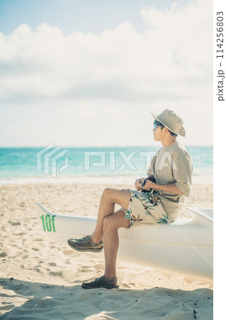 ハワイの砂浜で,ターコイズブルーの海をバックにウクレレをひく若い男性 114256803