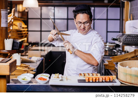 confident Asian chef is going to cut roll 114258279