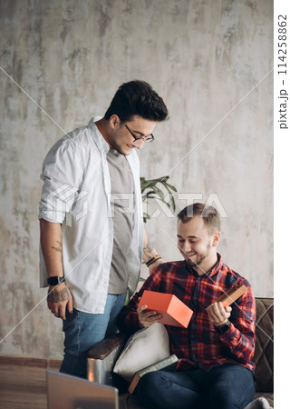 Happy surprised young handsome gay couple celebrating and giving gift at home Happy surprised young handsome gay couple celebrating and giving gift at home 114258862
