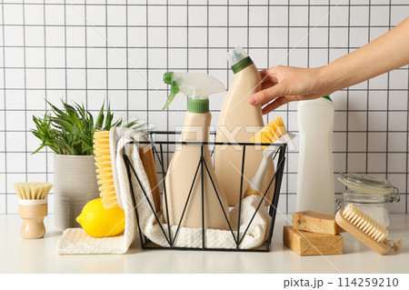 Basket with towel and bottles of detergents, hand, brushes and plant on light background 114259210