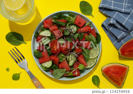 Fresh watermelon salad in a bowl with a glass of lemonade on a yellow background Fresh watermelon salad in a bowl with a glass of lemonade on a yellow background 114259458