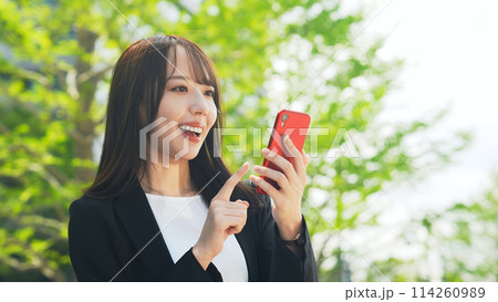 新緑を背景にスマホを使う女性ビジネスパーソン 114260989