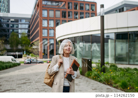 Mature businesswoman going home from work, enjoying beautiful weather and free time. Beautiful older woman with gray hair walking down city street. 114262150