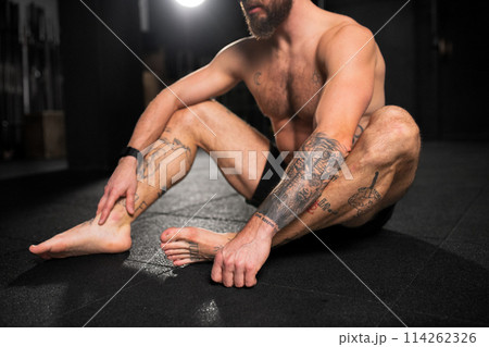 Barefoot muscular man resting on floor after training in gym. Routine workout for physical and mental health. Barefoot muscular man resting on floor after training in gym. Routine workout for physical and mental health. 114262326