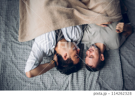 Handsome sleepy man with bristle kissing good night male partner lying in bed Handsome sleepy man with bristle kissing good night male partner lying in bed 114262328