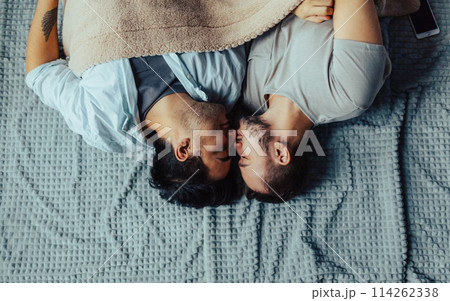 Handsome sleepy man with bristle kissing good night male partner lying in bed 114262338