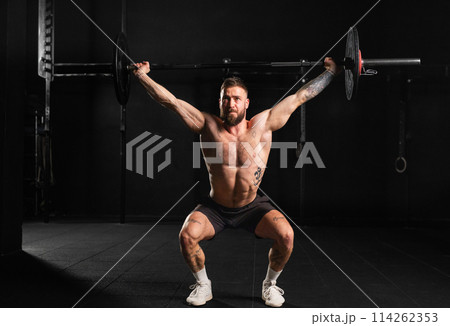 Strong man performing overhead squat pressing barbell up, full length shot. Routine workout for physical and mental health. Strong man performing overhead squat pressing barbell up, full length shot. Routine workout for physical and mental health. 114262353