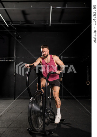 Man exercising on elliptical cross-trainer machine, wearing activewear. Routine workout for physical and mental health. 114262369