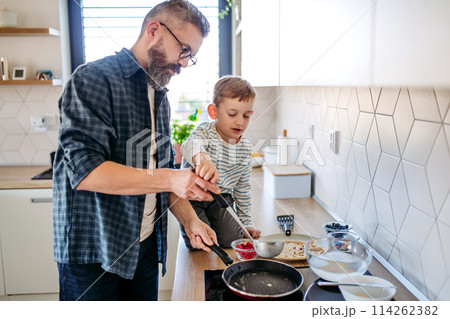 Boy helping father to make pancake. Father spending time with son at home, making snack together, cooking. Fathers day concept. Boy helping father to make pancake. Father spending time with son at home, making snack together, cooking. Fathers day concept. 114262382