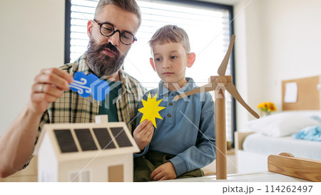 Father explaining renewable green energy, teaching son about sustainable lifestyle. Playing with model of house with solar panels, wind turibine at home. Learning through play. Father explaining renewable green energy, teaching son about sustainable lifestyle. Playing with model of house with solar panels, wind turibine at home. Learning through play. 114262497
