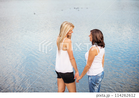Rear view of adult daughter spending time with her mother. Mom and daughter outdoors, on walk by reservoir, lake embankment. Unconditional, deep maternal love, Mother's Day concept.. 114262612