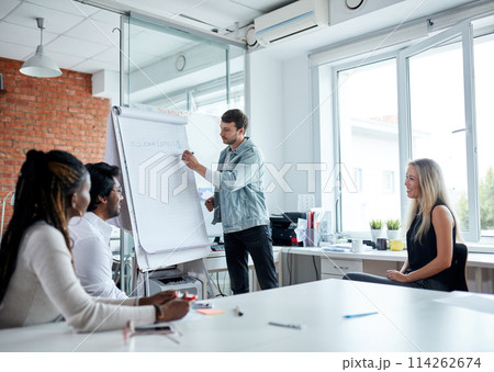 guy writing on the flipchart while his cheerful friends are looking at him guy writing on the flipchart while his cheerful friends are looking at him 114262674