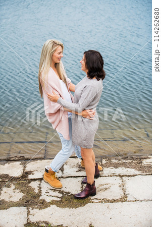 Mom and daughter on spring vacation together by lake. Mother and daugher together time in vacation resort. Unconditional, deep maternal love, Mother's Day concept. Mom and daughter on spring vacation together by lake. Mother and daugher together time in vacation resort. Unconditional, deep maternal love, Mother's Day concept. 114262680