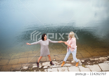 Adult daughter spending time with her mother, having fun, laughing. Mom and daughter outdoors, on walk by reservoir, lake embankment. Unconditional, deep maternal love, Mother's Day concept. 114262707