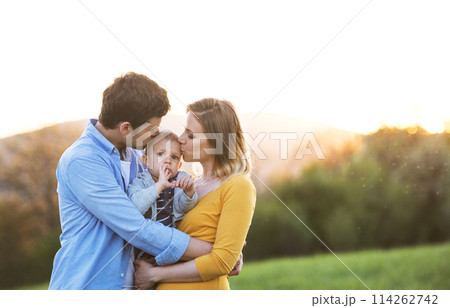 New parents holding small toddler, baby, outdoors in spring nature. Happy family moment New parents holding small toddler, baby, outdoors in spring nature. Happy family moment 114262742