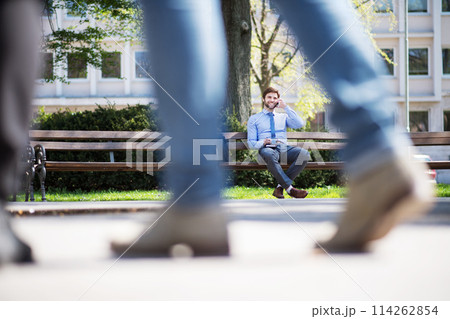 Handsome businessman phone calling on smartphone, sitting on city bench, writing notes. Working remotely, waiting for business meeting. Manager smiling, outdoor in urban setting Handsome businessman phone calling on smartphone, sitting on city bench, writing notes. Working remotely, waiting for business meeting. Manager smiling, outdoor in urban setting 114262854