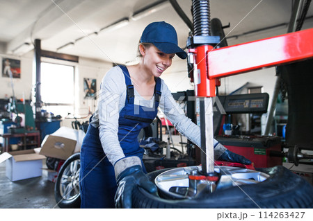 Female auto mechanic changing tieres in auto service, using machinery to removing tire. Beautiful woman working in garage. Female auto mechanic changing tieres in auto service, using machinery to removing tire. Beautiful woman working in garage. 114263427
